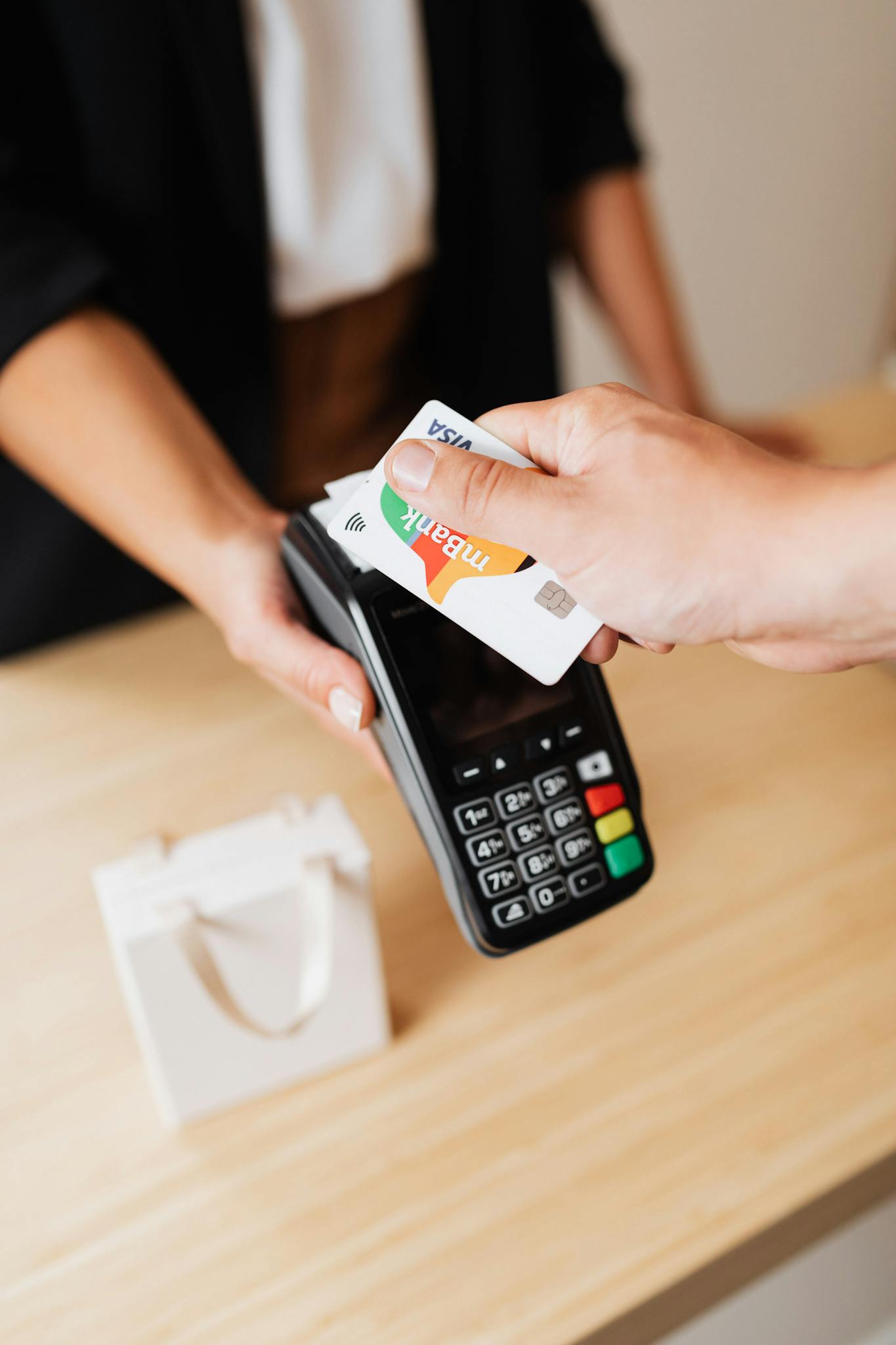 A person using a credit card for contactless payment at a retail counter.